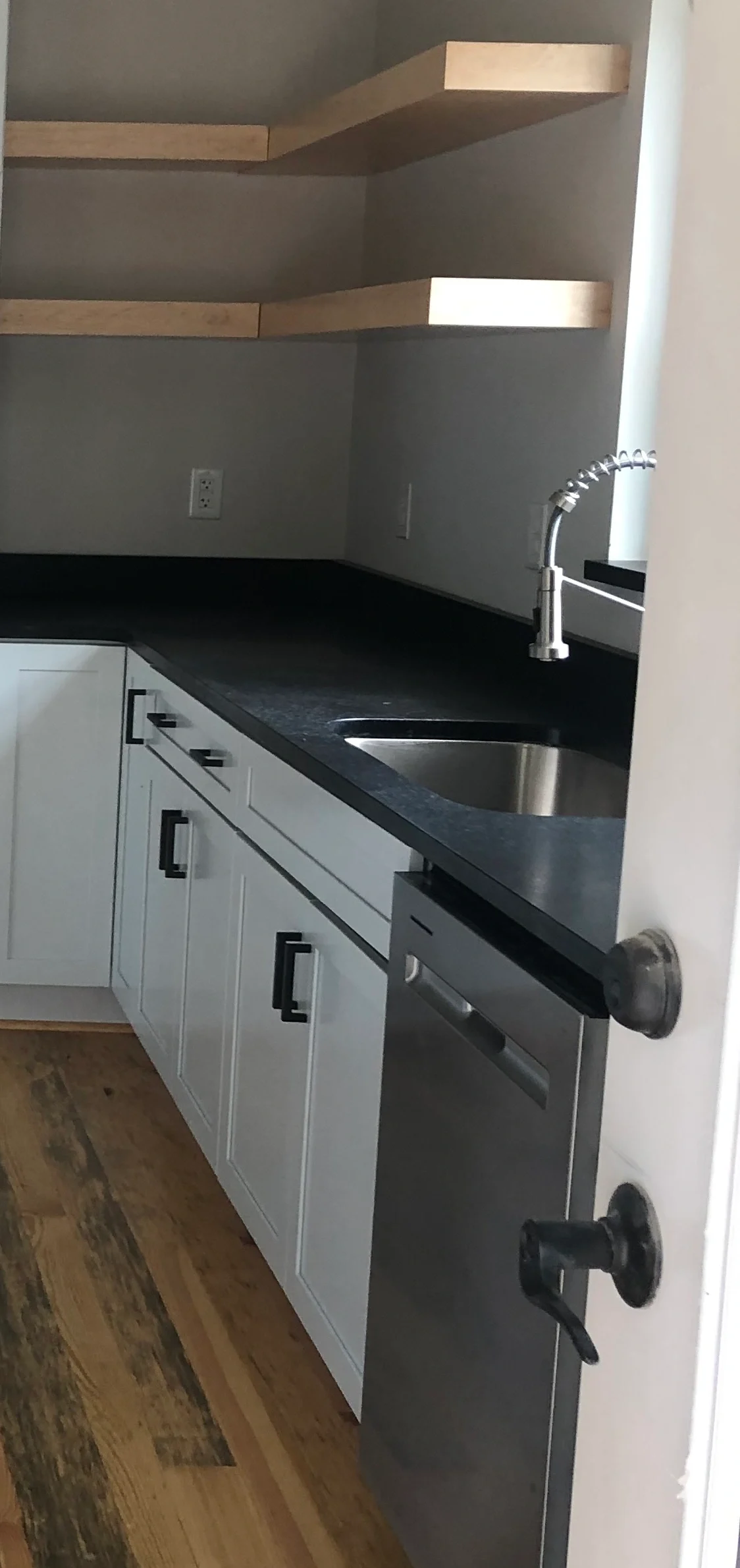 Open wood shelves above a kitchen sink and dark countertop
